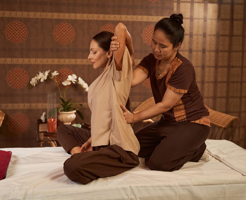 Female sitting on couch with her eyes closed during upper back stretch performed by masseuse