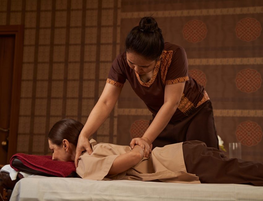 Concentrated serious Asian massotherapist applying pressure to affected muscle on patient shoulder